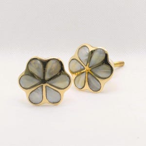 May include: A pair of flower-shaped cufflinks with a gold-colored border and a pearlescent, petal-like design. The cufflinks are set against a white background, highlighting their elegant design. These accessories are suitable for formal wear.