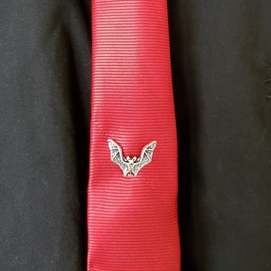 May include: A red silk tie with a silver bat tie clip. The tie is on a black shirt.