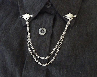 May include: A silver chain collar clip with two planet-shaped charms. The chain is double-stranded and the charms have a ring around them.
