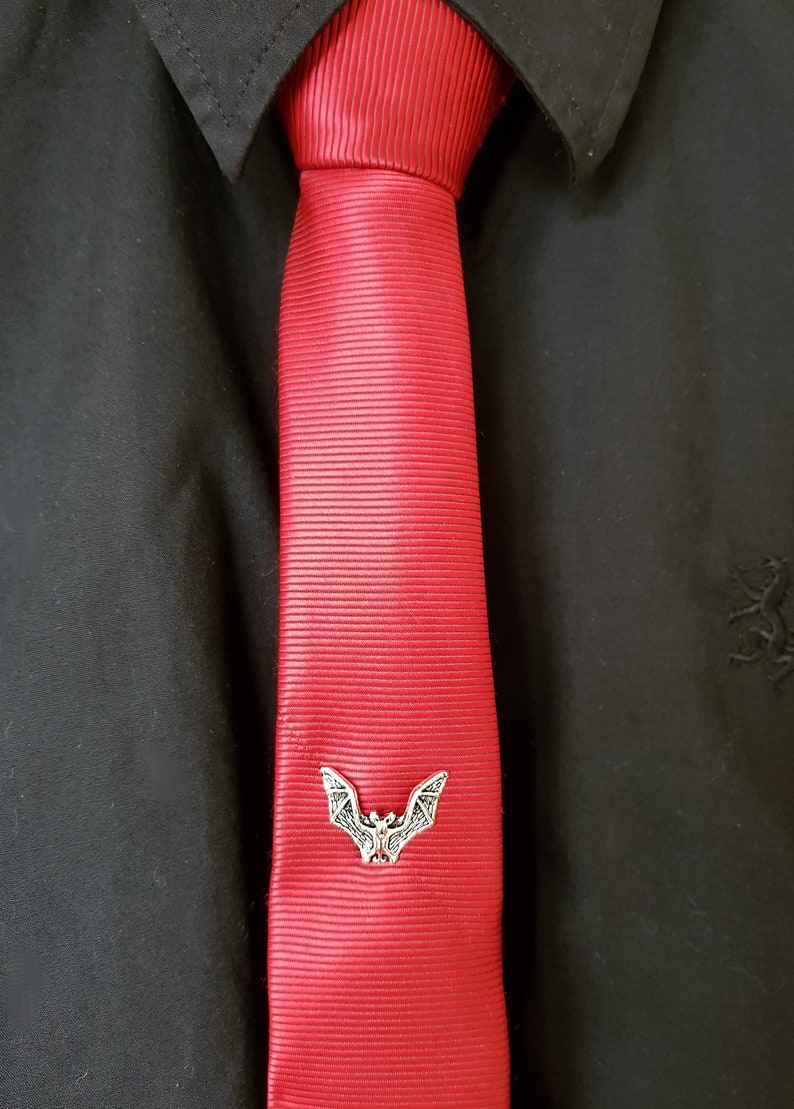 May include: A red silk tie with a silver bat tie clip. The tie is on a black shirt.