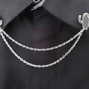 May include: A silver chain with two cactus-shaped charms attached to it. The chain is double-layered and has a delicate, linked design.