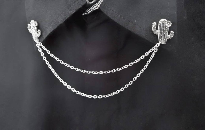 May include: A silver chain with two cactus-shaped charms attached to it. The chain is double-layered and has a delicate, linked design.