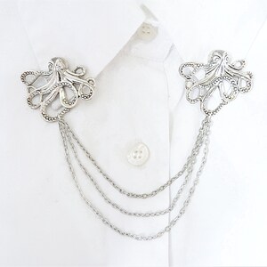 May include: Silver octopus brooch with a chain attached. The brooch is a decorative accessory for a shirt or jacket.