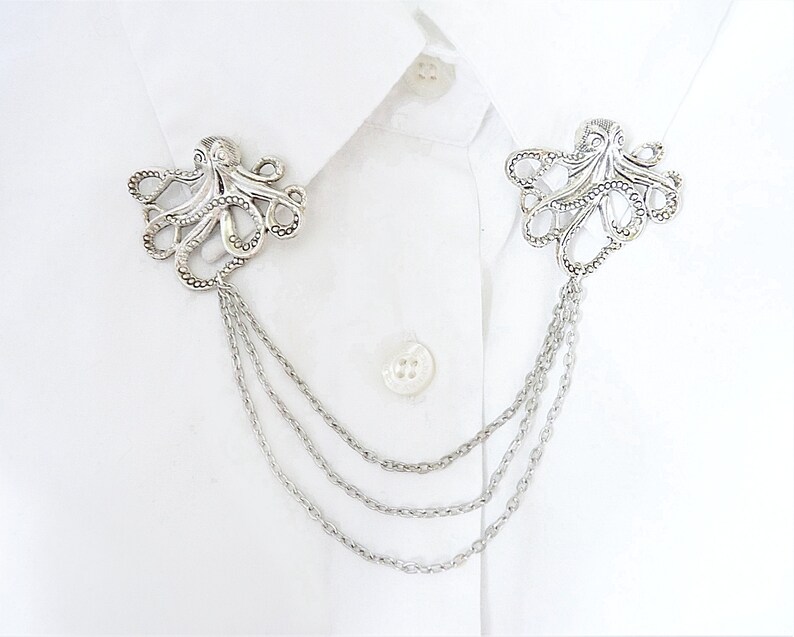 May include: Silver octopus brooch with a chain attached. The brooch is a decorative accessory for a shirt or jacket.