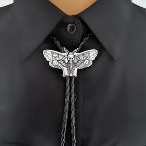 May include: A black leather bolo tie with a silver skull and moth pendant. The pendant is detailed with intricate wings and a skull face.