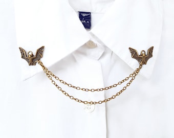 May include: A pair of gold-tone bat collar clips connected by a double chain. The clips are detailed with a bat design.