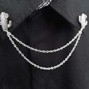 May include: A silver cactus-shaped collar pin with a double chain attached.