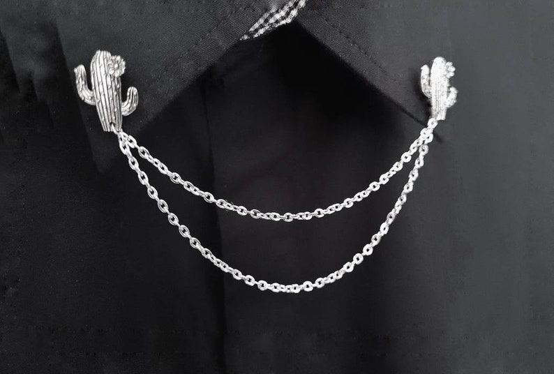 May include: A silver cactus-shaped collar pin with a double chain attached.