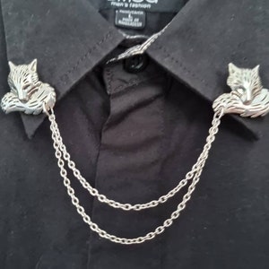 Puede incluir: Un broche de collar de cadena plateada con dos dijes de cabeza de zorro. La cadena es de doble cadena y las cabezas de zorro están mirando hacia adentro.
