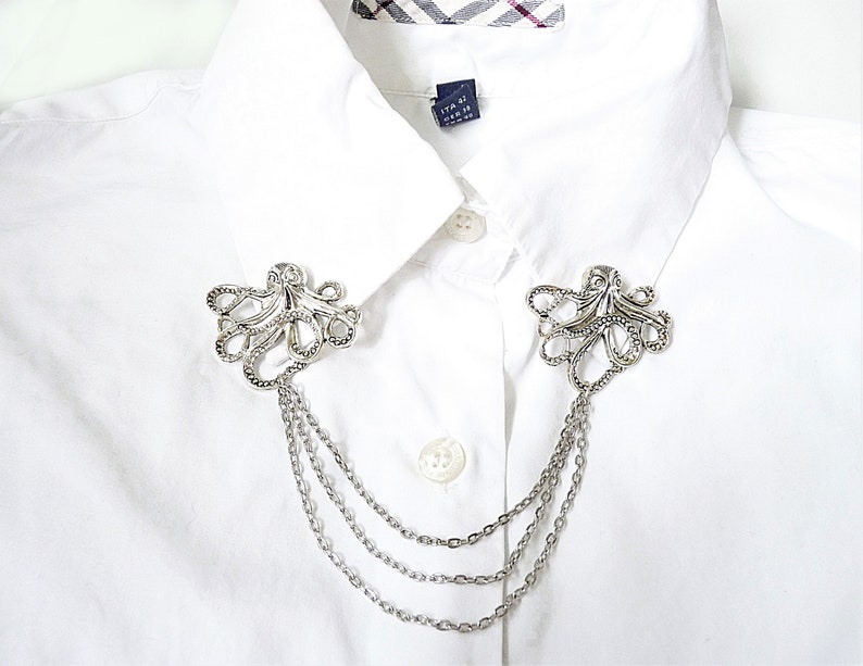 May include: Silver collar clip with a decorative octopus design and three chains. The clip is attached to a white shirt.
