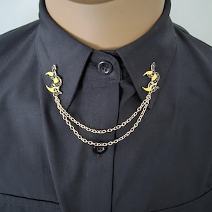 May include: A gold collar pin with a black and yellow crescent moon design, connected by a double chain.