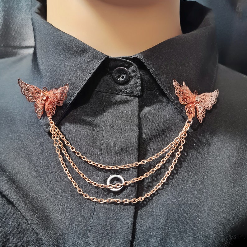 May include: A gold-toned chain necklace with two butterfly charms. The butterflies are delicate and intricate, with a filigree design. The chain is layered, creating a multi-strand look.