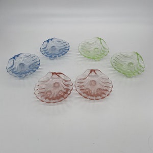 May include: Six small glass dishes shaped like seashells in blue, green, and pink.
