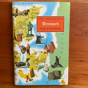 Puede incluir: Una portada de libro de viajes vintage titulada "Dinamarca" del "Around the World Program" de la American Geographical Society. La portada presenta un mapa ilustrado colorido de Dinamarca con varios puntos de referencia e ilustraciones, incluyendo un molino de viento y la estatua de la Sirenita.