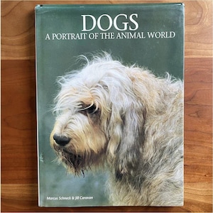 May include: A book cover with the title "DOGS A PORTRAIT OF THE ANIMAL WORLD" and a picture of a light-colored, shaggy dog. The cover is green with white text. The author's names are at the bottom.