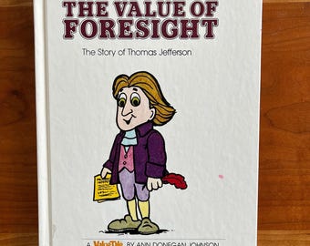 Può includere: Un libro per bambini intitolato "The Value of Foresight" con il sottotitolo "The Story of Thomas Jefferson". La copertina presenta un'illustrazione a cartoni animati di Thomas Jefferson con un cappotto viola, che tiene in mano un documento e una penna.