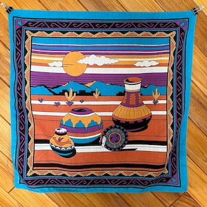 Peut inclure: Un bandana carré turquoise avec un motif de paysage désertique du Sud-Ouest. Le motif présente un coucher de soleil, des montagnes, des cactus et des poteries dans des tons orange, violet et jaune. La bordure est noire avec des motifs géométriques.