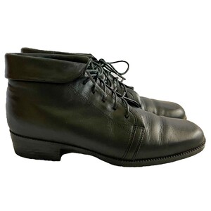 May include: A pair of black leather ankle boots featuring a folded cuff at the top, a rounded toe, and a lace-up closure with matching black laces. The boots have a low, stacked heel and a textured rubber outsole for traction and stability.