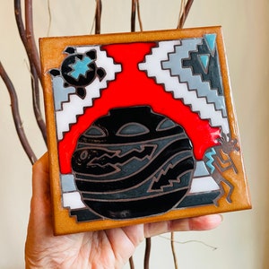 May include: A square ceramic tile with a Southwestern design. The tile features a black and white pot with a red background, a turquoise turtle, and a stylized figure in brown and turquoise.