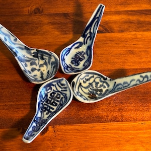 May include: Four blue and white porcelain spoons with Chinese characters and floral designs. The spoons are arranged in a star shape on a wooden surface.