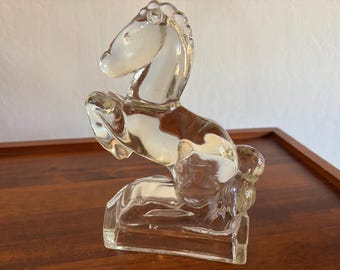 May include: A clear glass horse figurine in a rearing pose. The sculpture is detailed with a flowing mane and tail, and is mounted on a rectangular base. The horse is made of transparent glass.