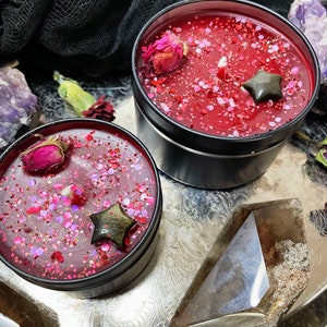 May include: Two red candles with black lids and glitter. The candles have dried rose petals and black star-shaped charms inside.