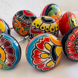 May include: A collection of round ceramic drawer knobs featuring vibrant, hand-painted floral patterns in red, yellow, blue, green, and black. Each knob has a smooth, glossy finish and includes a metal bolt and nut hardware for installation.