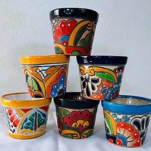 Puede incluir: Una pila de seis macetas de cerámica pintadas a mano. Cada maceta presenta un diseño único con colores vibrantes, incluyendo rojo, amarillo, azul y verde. Las macetas tienen un acabado brillante y son adecuadas para uso en interiores o exteriores.