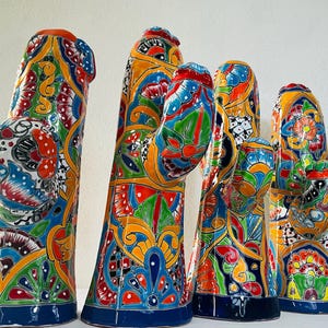 May include: Four ceramic cactus sculptures featuring vibrant, hand-painted Talavera-style patterns in shades of blue, yellow, red, green, and white. Each piece displays intricate floral and geometric motifs across the entire surface of the cactus.