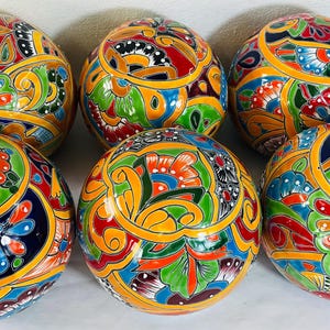 May include: A set of five spherical ceramic objects featuring a glossy finish and intricate hand-painted floral patterns in vibrant shades of orange, yellow, green, blue, and red against a dark blue background, arranged in a cluster.