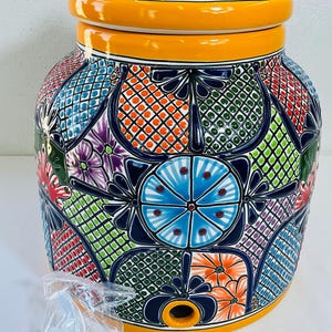Puede incluir: Un dispensador de agua de cerámica grande y redondo con un patrón vibrante pintado a mano de formas geométricas, flores y diseños de cuadrícula en azul, naranja, verde y morado. Incluye una tapa a juego y un grifo de plástico blanco separado.