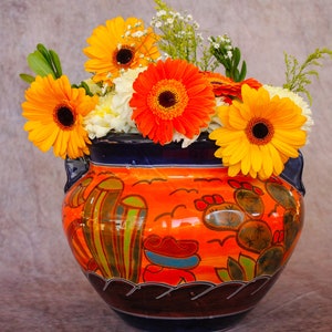 May include: A colorful ceramic vase with a southwestern design, filled with a bouquet of orange, yellow, and white flowers.