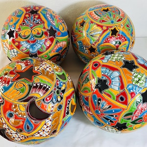 May include: Four spherical ceramic globes featuring a vibrant, multi-colored hand-painted pattern with floral and geometric motifs. Each globe is punctuated by several star-shaped and crescent-shaped cutouts across the glossy, glazed surface.