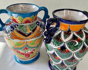 May include: Two colourful ceramic vases with handles. The vase on the left has a blue, orange, green and red floral pattern. The vase on the right has a blue, green, orange and white pattern with a scale-like design.