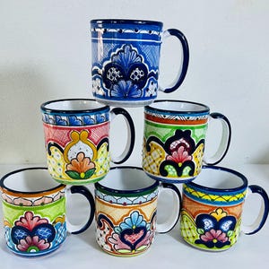 Puede incluir: Una colección de seis tazas de cerámica dispuestas en una pila piramidal. Cada taza presenta un patrón único pintado a mano con intrincados motivos florales y geométricos en tonos azul, rojo, amarillo, verde y naranja sobre base blanca.