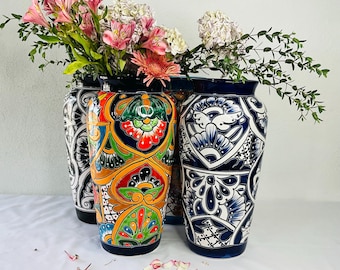 May include: Three colourful ceramic vases with intricate floral patterns. The vases are decorated with blue, white, yellow, orange, red and green paint. The vases are arranged in a row on a white surface.