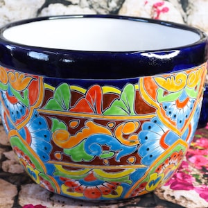 May include: A blue ceramic planter with colorful floral designs and two handles. The planter is decorated with bright colors, including yellow, orange, green, and blue.