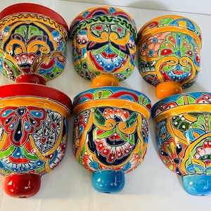 May include: A set of six ceramic wall planters featuring vibrant, hand-painted floral and geometric patterns in red, yellow, blue, green, and orange. Each bowl-shaped planter has a wide rim and a small, solid-colored knob at the base.