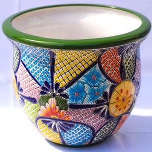 May include: A large, round, ceramic planter with a green rim and a colorful floral pattern. The pattern includes blue, green, yellow, pink, and orange flowers and geometric shapes.