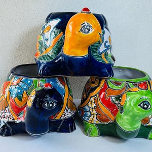 May include: Three ceramic turtle planters. The turtles have colorful, hand-painted designs on their shells. One turtle is blue with orange and white accents, another is green with red and orange, and the third is blue with yellow and white.