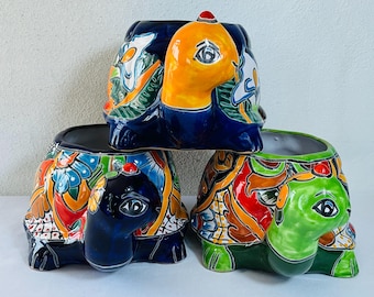 May include: Three ceramic turtle planters. The turtles have colorful, hand-painted designs on their shells. One turtle is blue with orange and white accents, another is green with red and orange, and the third is blue with yellow and white.