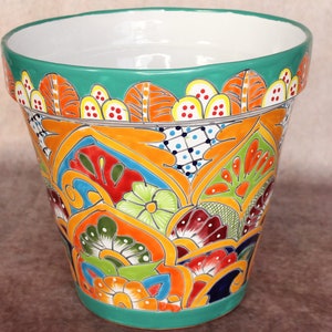 May include: A vibrant, hand-painted ceramic flower pot. The pot features a teal rim and base, with a colorful design of orange, yellow, green, and red floral patterns. The interior is white, and the pot is suitable for indoor or outdoor use.