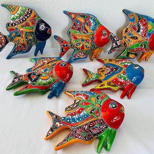 May include: A collection of six ceramic fish wall decorations, each featuring vibrant, hand-painted floral and geometric patterns in bright colors including red, blue, green, orange, and yellow, with glossy finishes and distinct fin shapes.
