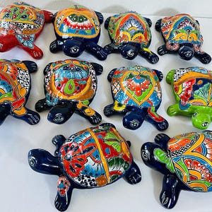 Könnte beinhalten: Eine Sammlung von zehn Keramik-Schildkrötenfiguren, jede mit glänzender Oberfläche und komplexen, handbemalten Mustern auf den Panzern. Die Schildkröten haben dunkelblaue, rote oder grüne Körper mit lebendigen floralen und geometrischen Designs.