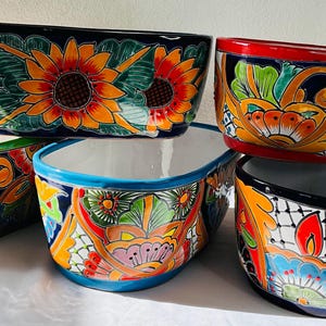 May include: Five colourful oval ceramic planters with floral designs. The planters are stacked on top of each other. The designs include sunflowers, paisley patterns, and geometric shapes.