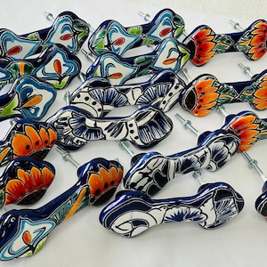 Peut inclure: Une collection de 18 poignées de tiroir en céramique colorées avec des motifs floraux. Les poignées sont peintes dans des tons de bleu, blanc, orange et jaune. Chaque poignée présente un motif floral unique et est fixée à une vis en métal argenté.