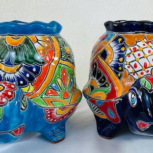 May include: Two ceramic turtle planters with vibrant, hand-painted designs. The turtles feature blue, orange, green, and yellow floral patterns. The planters have a scalloped rim and are suitable for indoor or outdoor use.