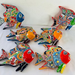 Puede incluir: Colección de seis esculturas de peces de cerámica coloridas. Cada pez presenta un diseño único con colores vibrantes, incluyendo rojo, azul, amarillo y verde. Los peces tienen patrones detallados y son probablemente artículos decorativos.