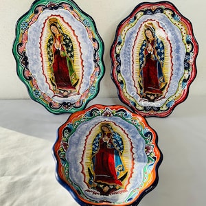 Puede incluir: Tres cuencos ovalados de cerámica con bordes festoneados, cada uno con una representación colorida de la Virgen María. Los cuencos están pintados en tonos vibrantes de azul, verde, rojo, amarillo y naranja, con intrincados diseños florales.