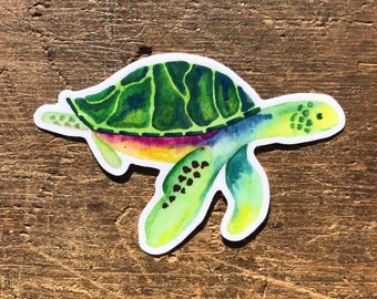 May include: A watercolor illustration of a green sea turtle with a rainbow shell. The turtle is swimming to the right and has a yellow spot on its head.